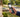 A hand holding an open modern flip phone displaying navigation on a suburban street.
